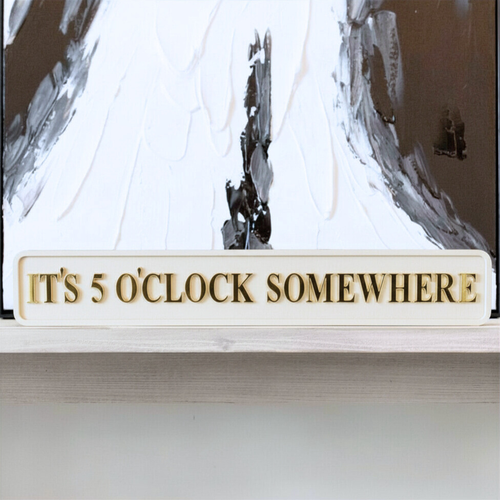 Decorative sign with 'IT'S 5 O'CLOCK SOMEWHERE' text in front of a abstract painting.
