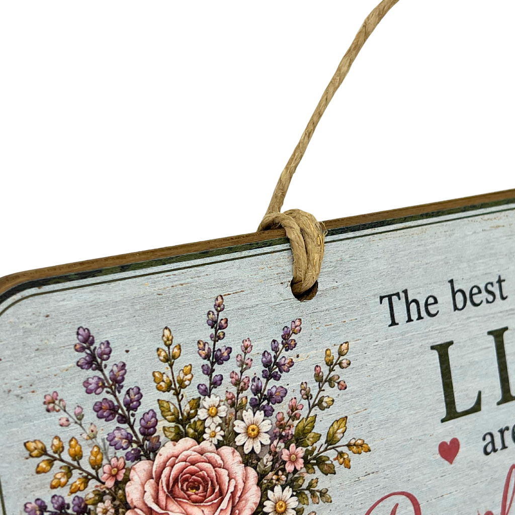 A close-up of a decorative hanging sign with a rustic whitewashed wood background, floral illustration featuring a pink rose and purple flowers, and partial printed text reading 'The best LI.