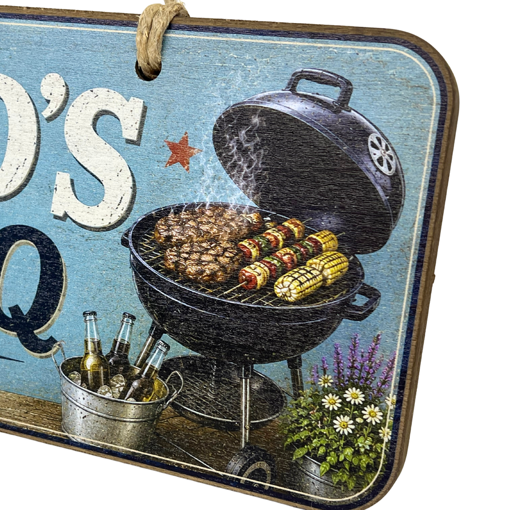 A rectangular decorative sign with rounded corners featuring a rustic barbecue scene. The sign has a weathered light blue background, a hanging rope at the top, and printed graphics of a black grill with meat and corn, a bucket of beer bottles, and flowers.