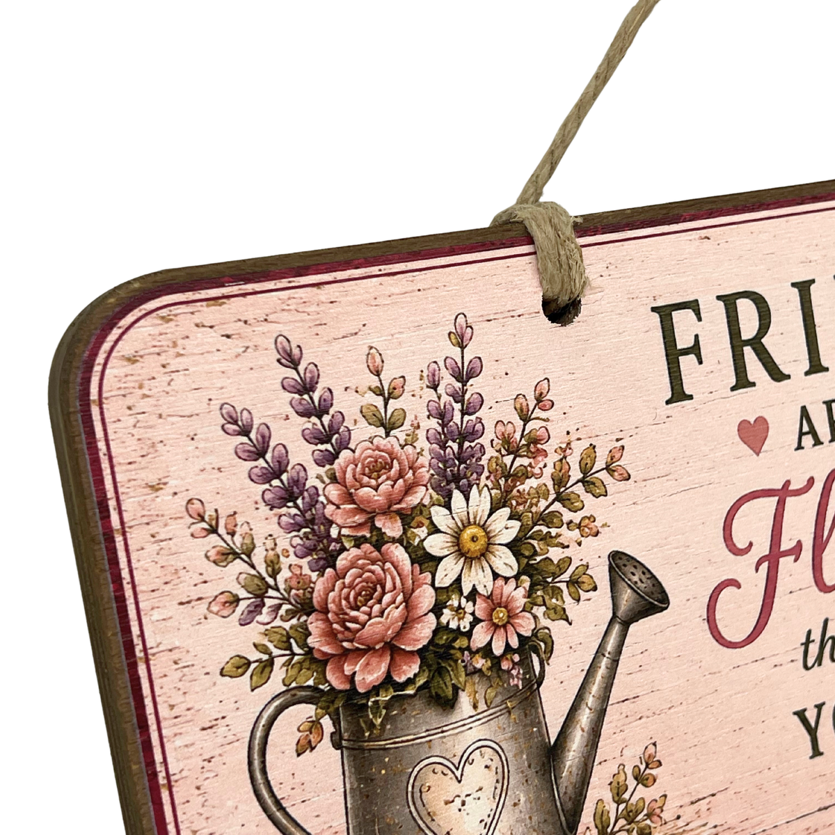 A close-up of a decorative hanging sign with a rustic pink background, floral illustration in a metal watering can, and partial text reading 'FRI.