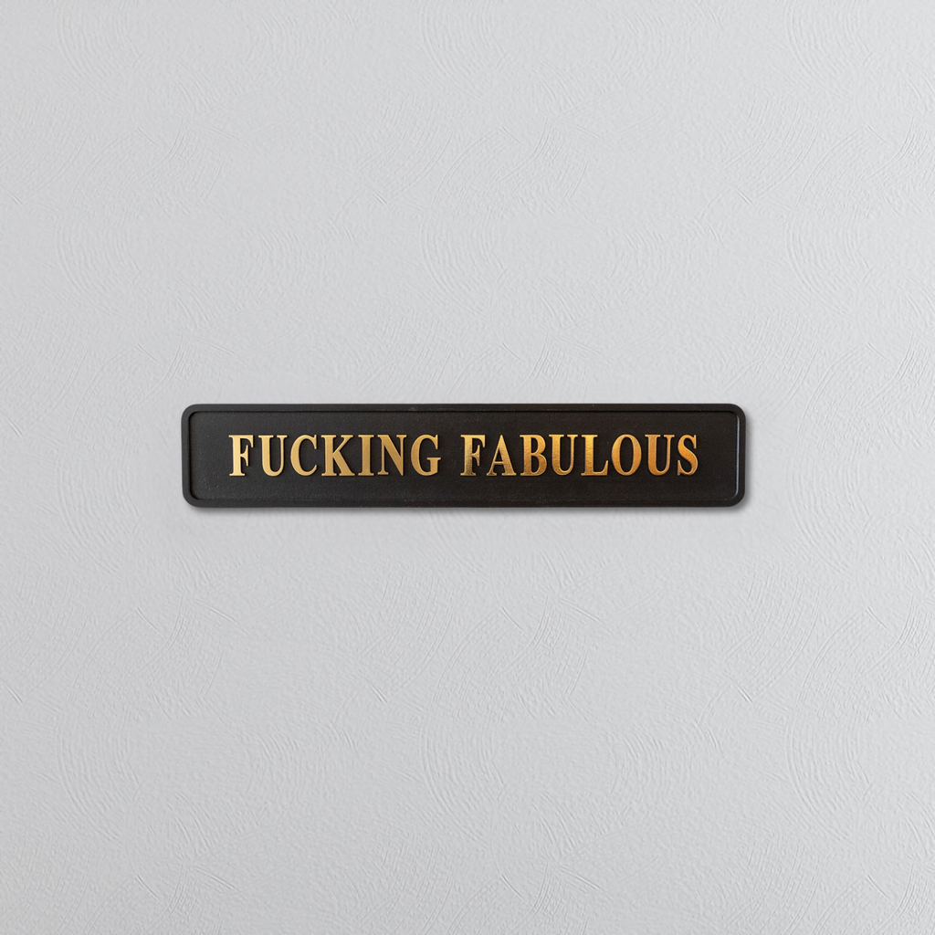 Black rectangular sign with 'FUCKING FABULOUS' in gold letters on a light gray background