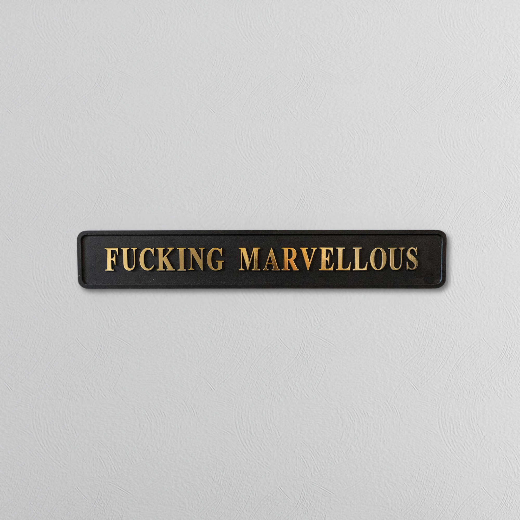 Rectangular sign with 'FUCKING MARVELLOUS' gold text on a light gray background