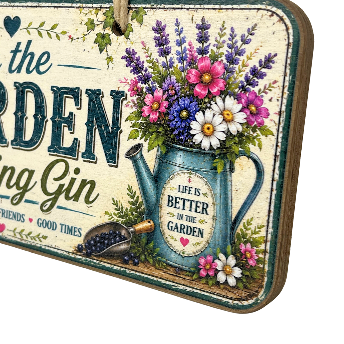 A rectangular decorative garden sign with a rustic distressed cream background and a hanging loop at the top. The sign features large dark teal lettering, a blue watering can filled with colorful flowers, green foliage, and smaller decorative text including 'LIFE IS BETTER IN THE GARDEN' 