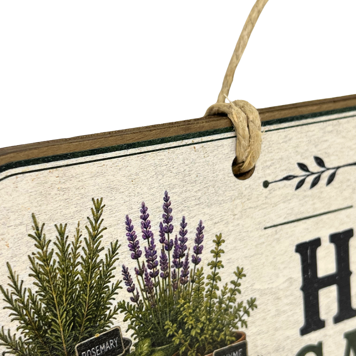 Close-up of a decorative hanging sign with a rope loop, showing botanical illustrations of green and purple herbs on a textured cream background with partial black lettering.
