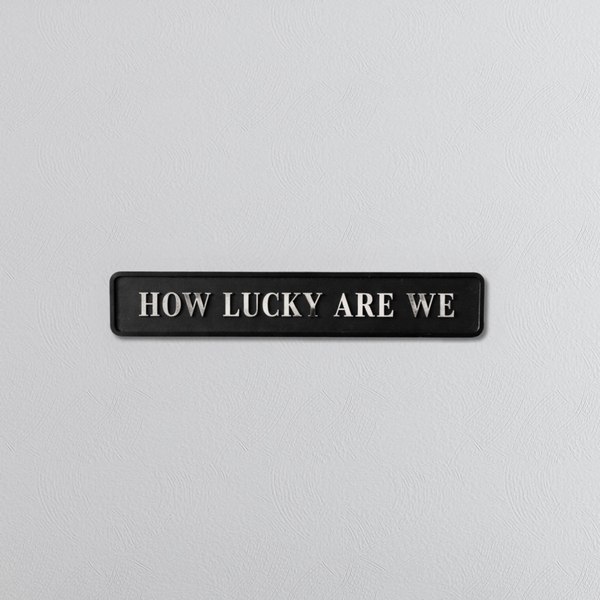 Black decorative sign with HOW LUCKY ARE WE silver text 