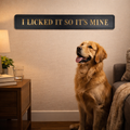 Dog sitting in a living room with a humorous sign above it 'I licked it so it's mine'