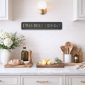 Kitchen counter with decor items and a sign reading 'I was born this gay' on a tiled wall.