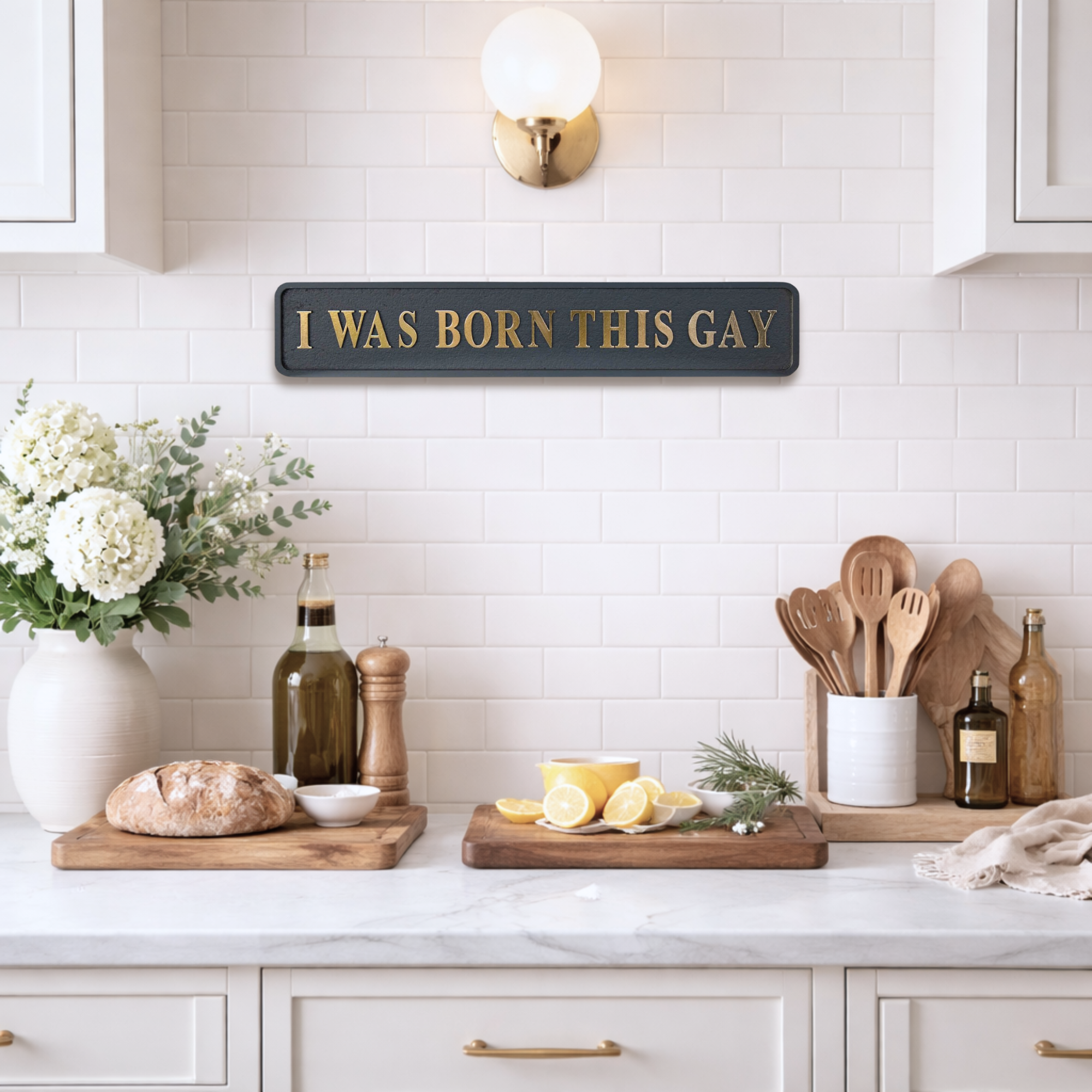 Kitchen counter with decor items and a sign reading 'I was born this gay' on a tiled wall.