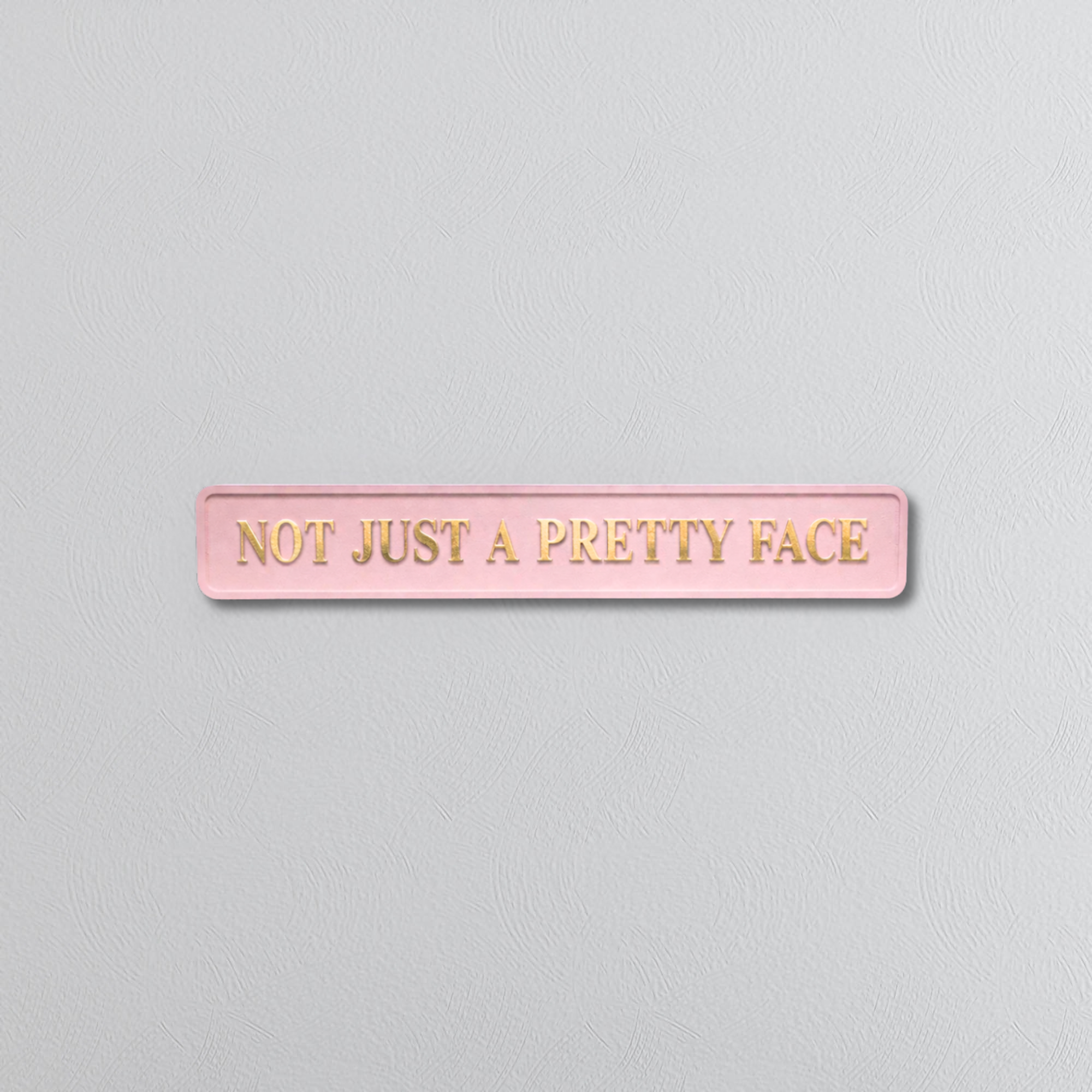 pink decorative sign with NOT JUST A PRETTY FACE gold text 