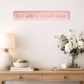 pink decorative sign with NOT JUST A PRETTY FACE gold text in a stylish living room setting