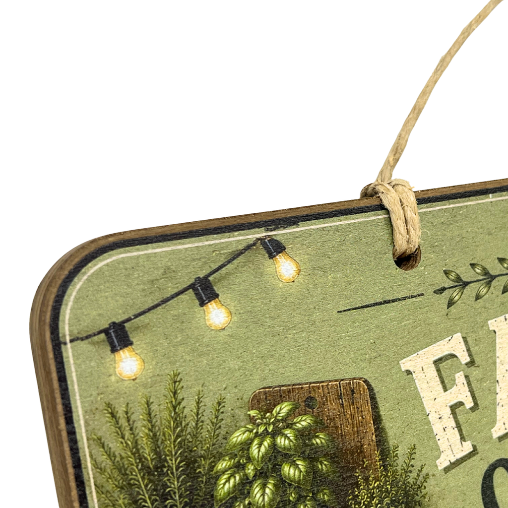 Close-up of a rustic decorative sign with a hanging twine loop, showing part of a green printed design with string lights, pinecones, foliage, and white lettering on a white background.