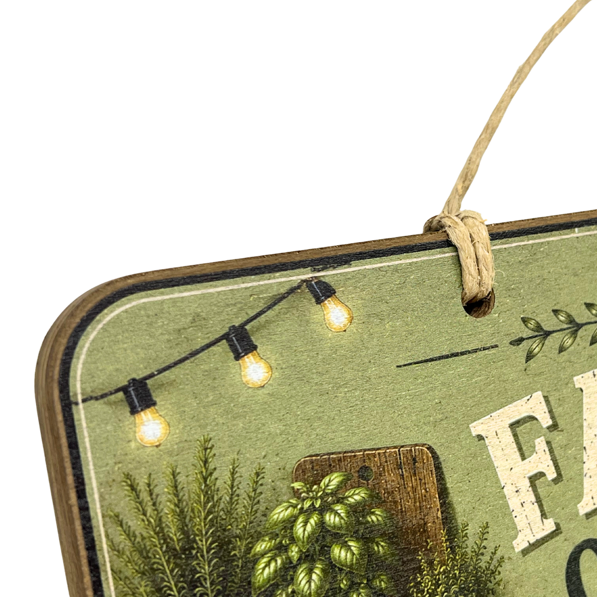 Close-up of a rustic decorative sign with a hanging twine loop, showing part of a green printed design with string lights, pinecones, foliage, and white lettering on a white background.