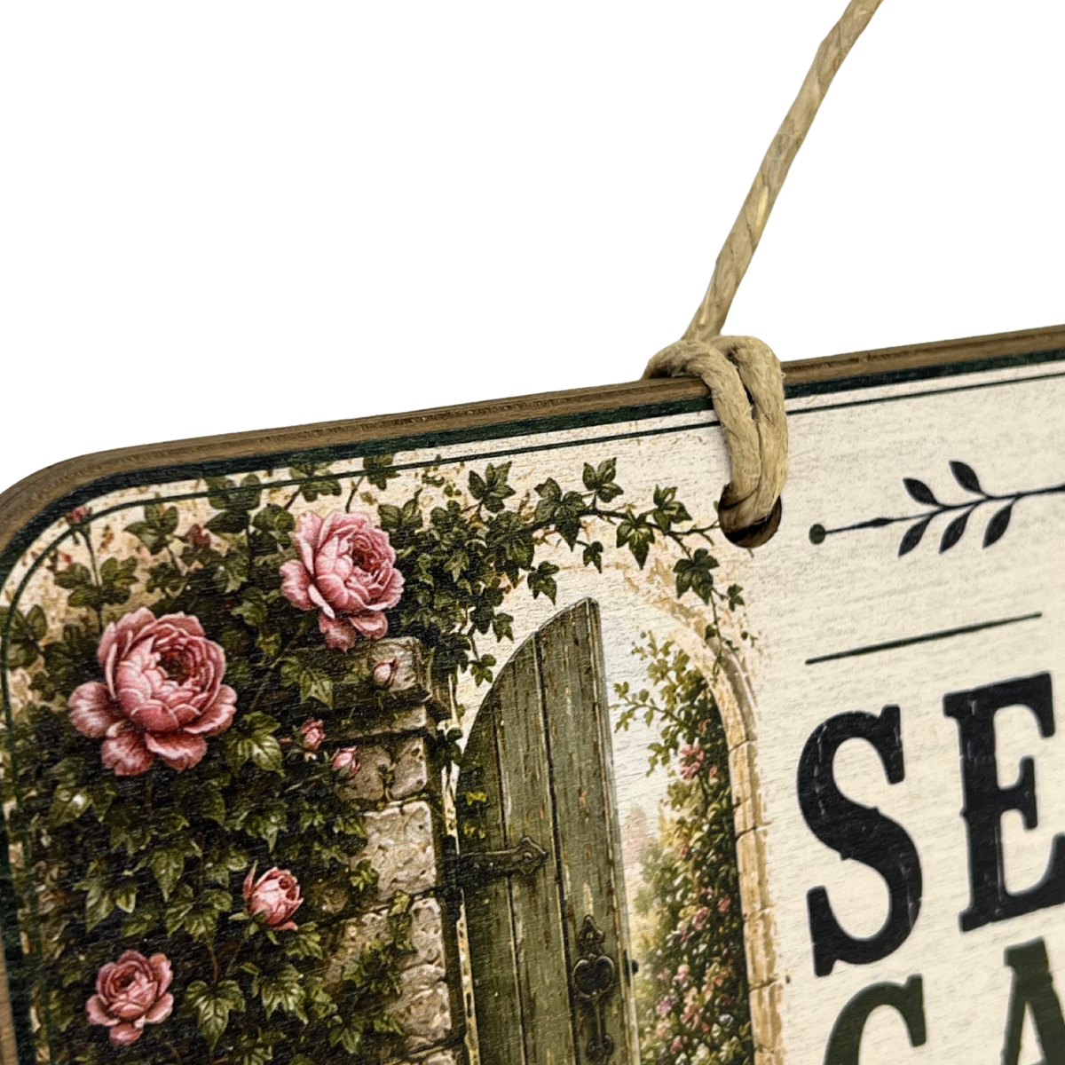 A decorative hanging sign with a rustic vintage design, featuring pink roses, green ivy, a weathered wooden door, and partial black text on a distressed cream background. The sign has a natural twine loop at the top and is photographed against a plain white background.
