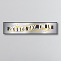 Decorative mirror sign with gold text 'SOUNDS GAY, I'M IN' in an art deco style on a gray background