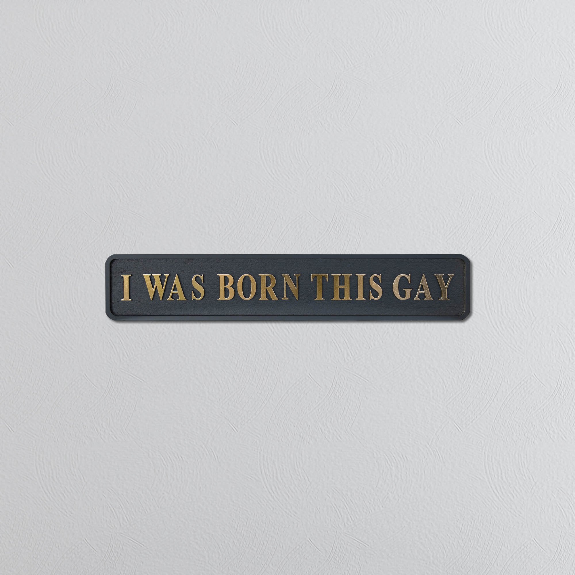 Plaque with 'I WAS BORN THIS GAY' in gold text on a light gray background