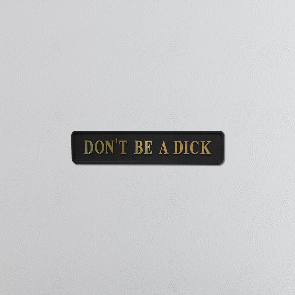 Rectangular sign with 'DON'T BE A DICK' in gold text on a light gray background