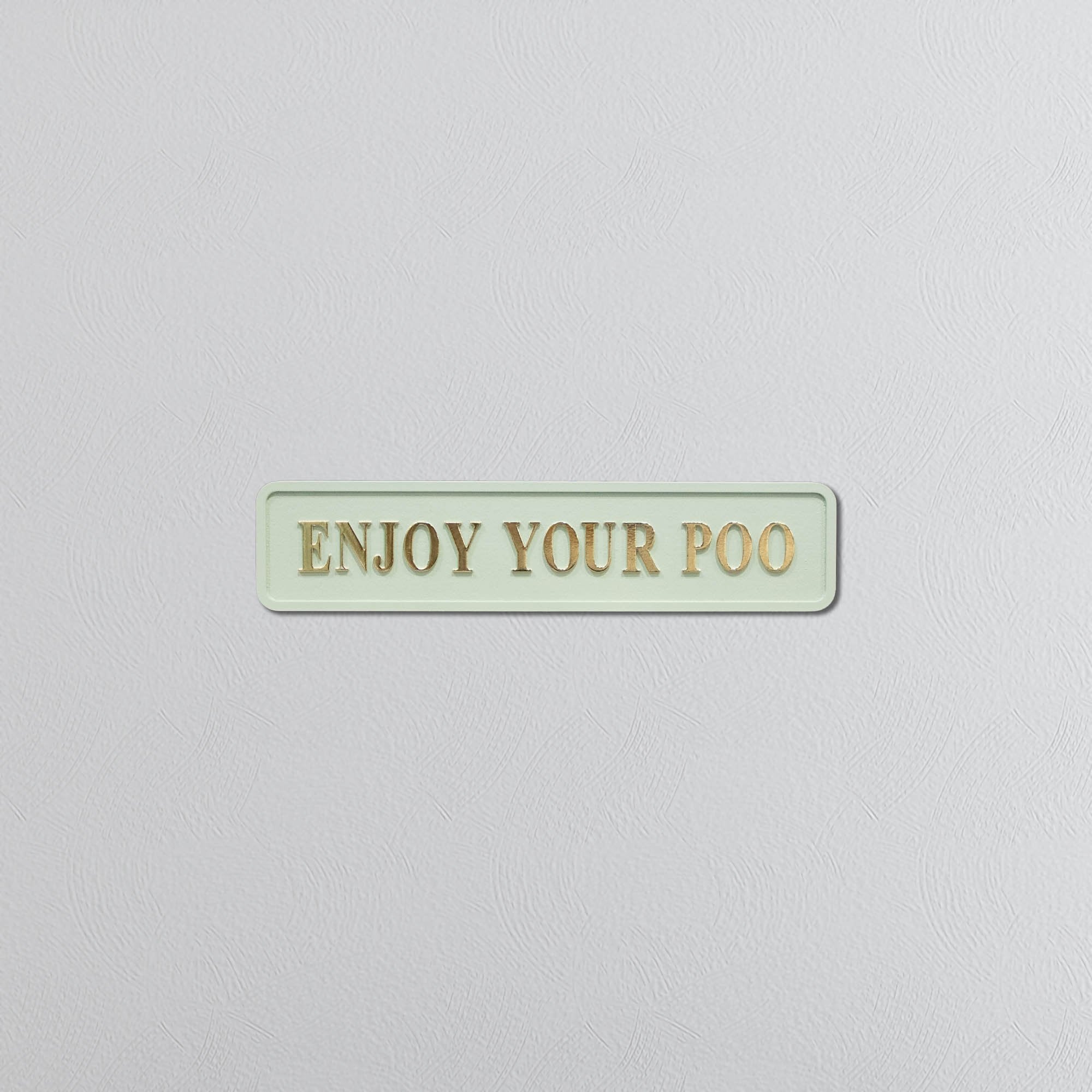 Rectangular sage green sign with 'ENJOY YOUR POO' gold text on a light gray background