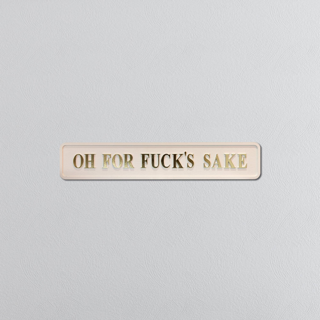 Rectangular cream sign with gold text reading 'OH FOR FUCK'S SAKE' on a gray background