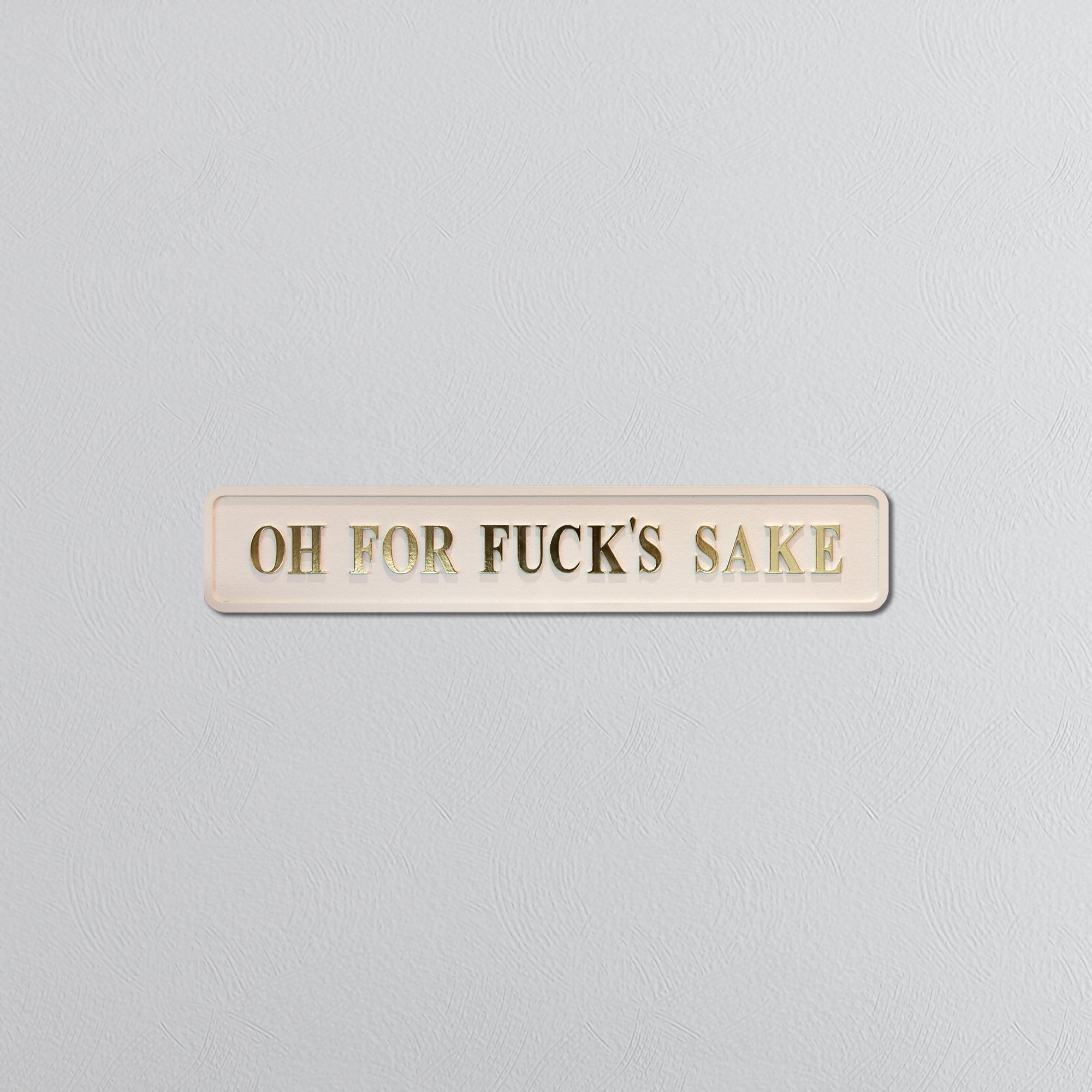 Rectangular cream sign with gold text reading 'OH FOR FUCK'S SAKE' on a gray background