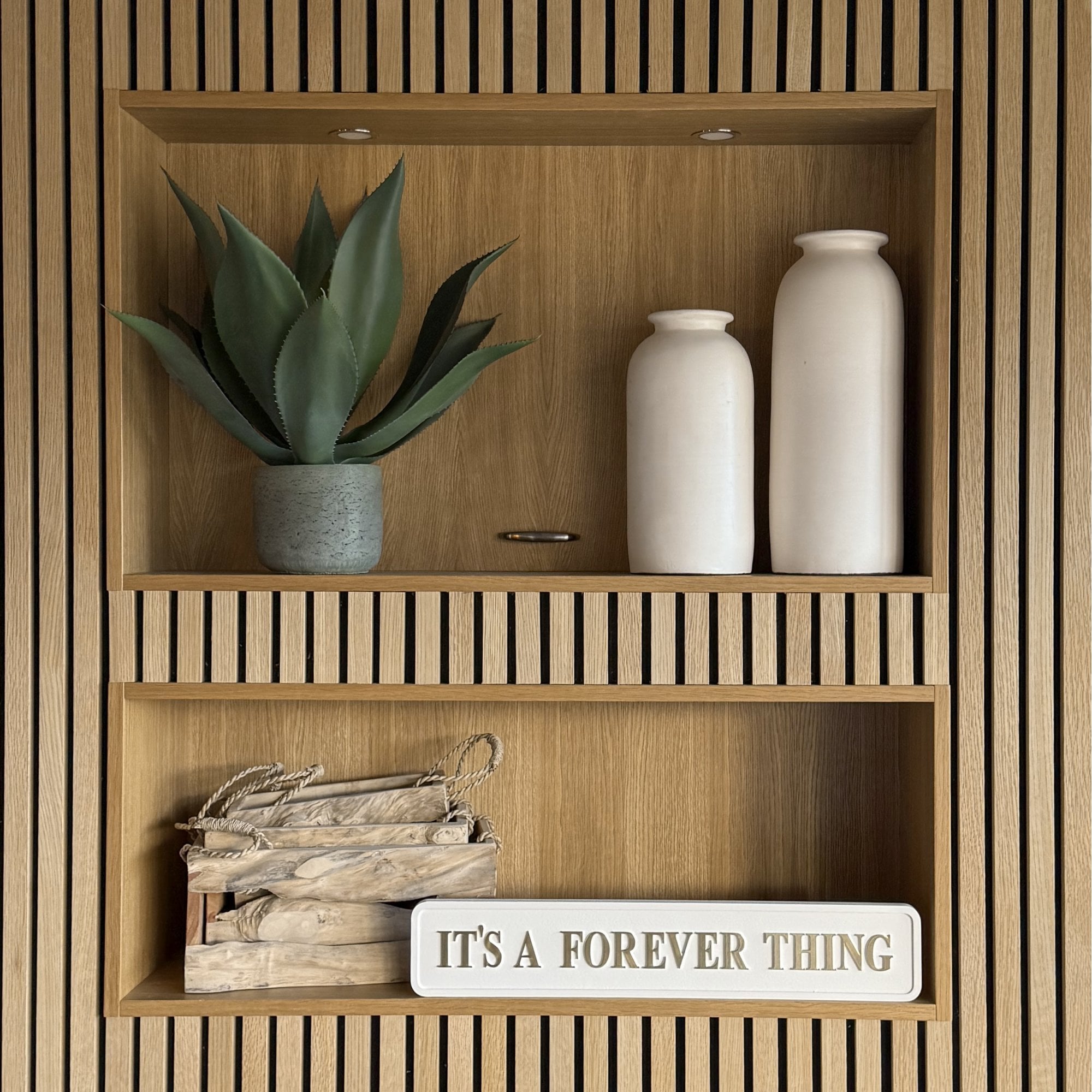Wooden shelves with decorative items including a plant, vases, and a cream sign with gold text saying IT'S A FOREVER THING