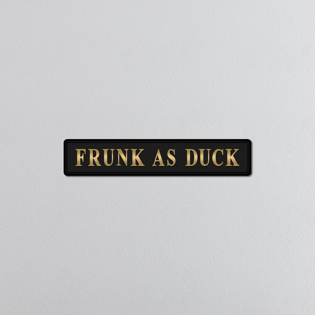 Black sign with gold text 'FRUNK AS DUCK' on a light gray background