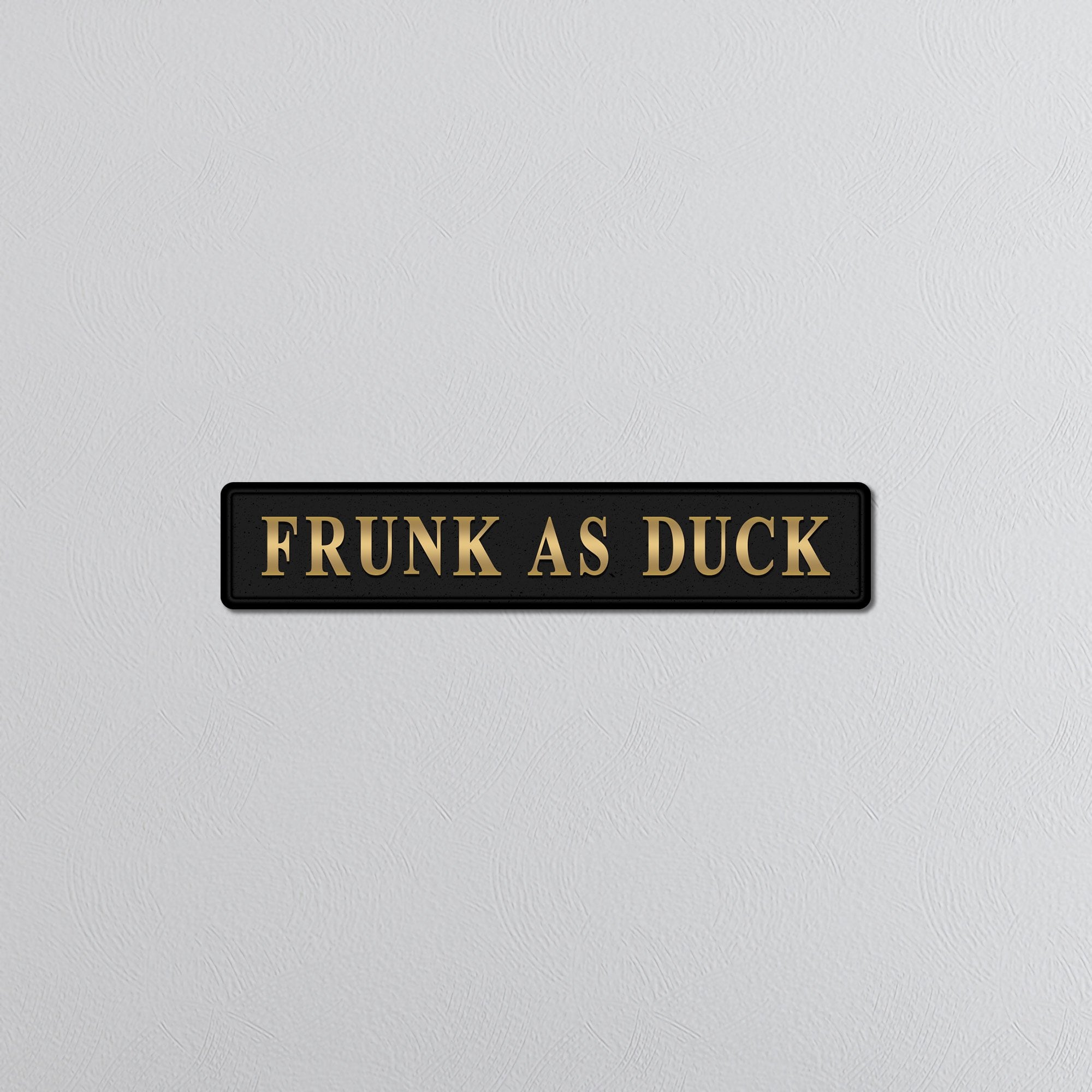 Black sign with gold text 'FRUNK AS DUCK' on a light gray background