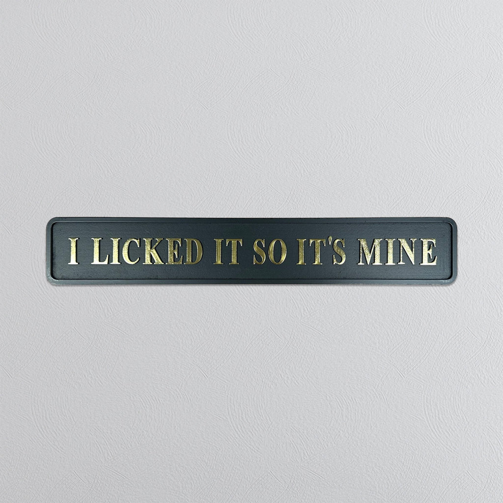 Black sign with gold text 'I LICKED IT SO IT'S MINE' on a light gray background