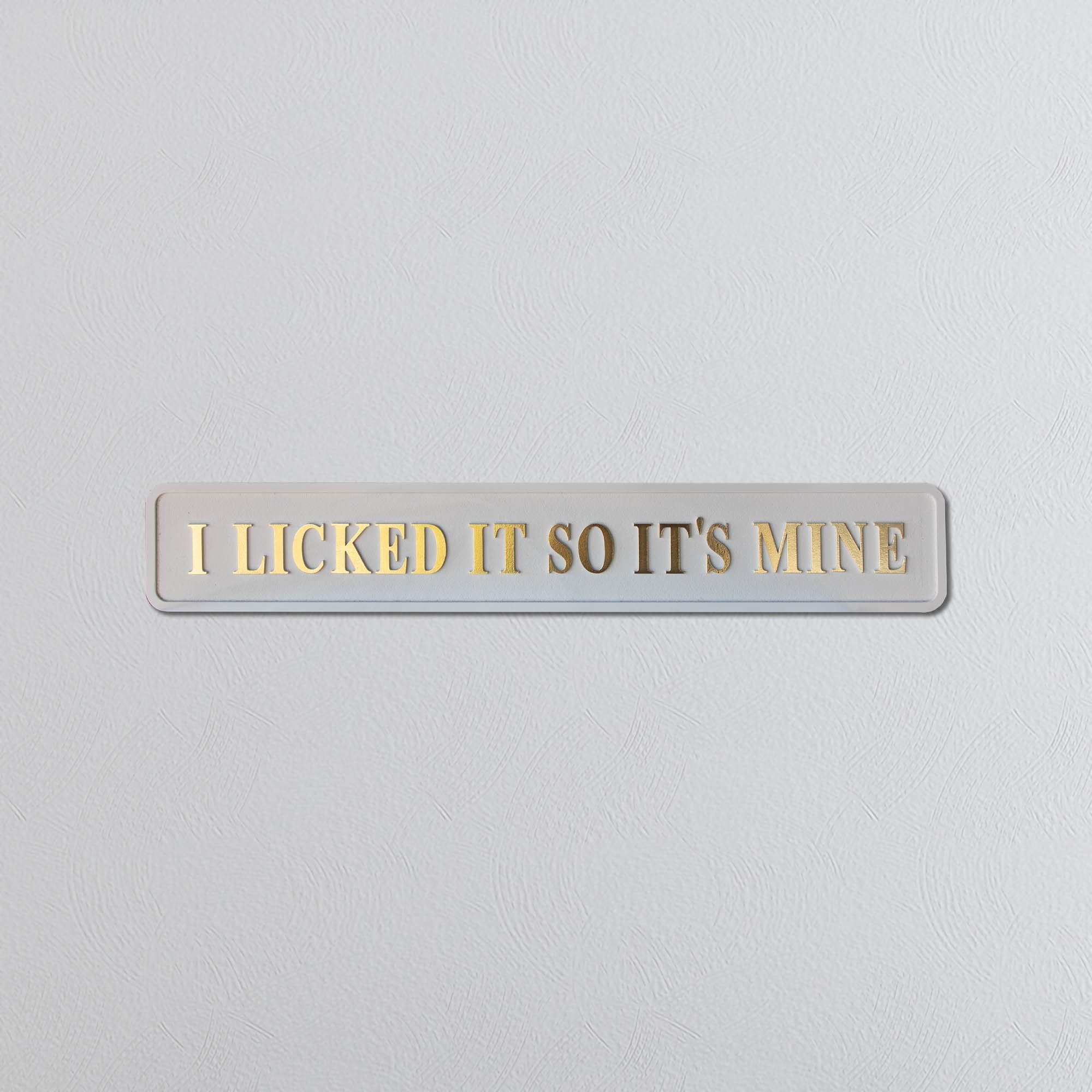 Wooden plaque with 'I Licked It So It's Mine' gold text on a light gray background