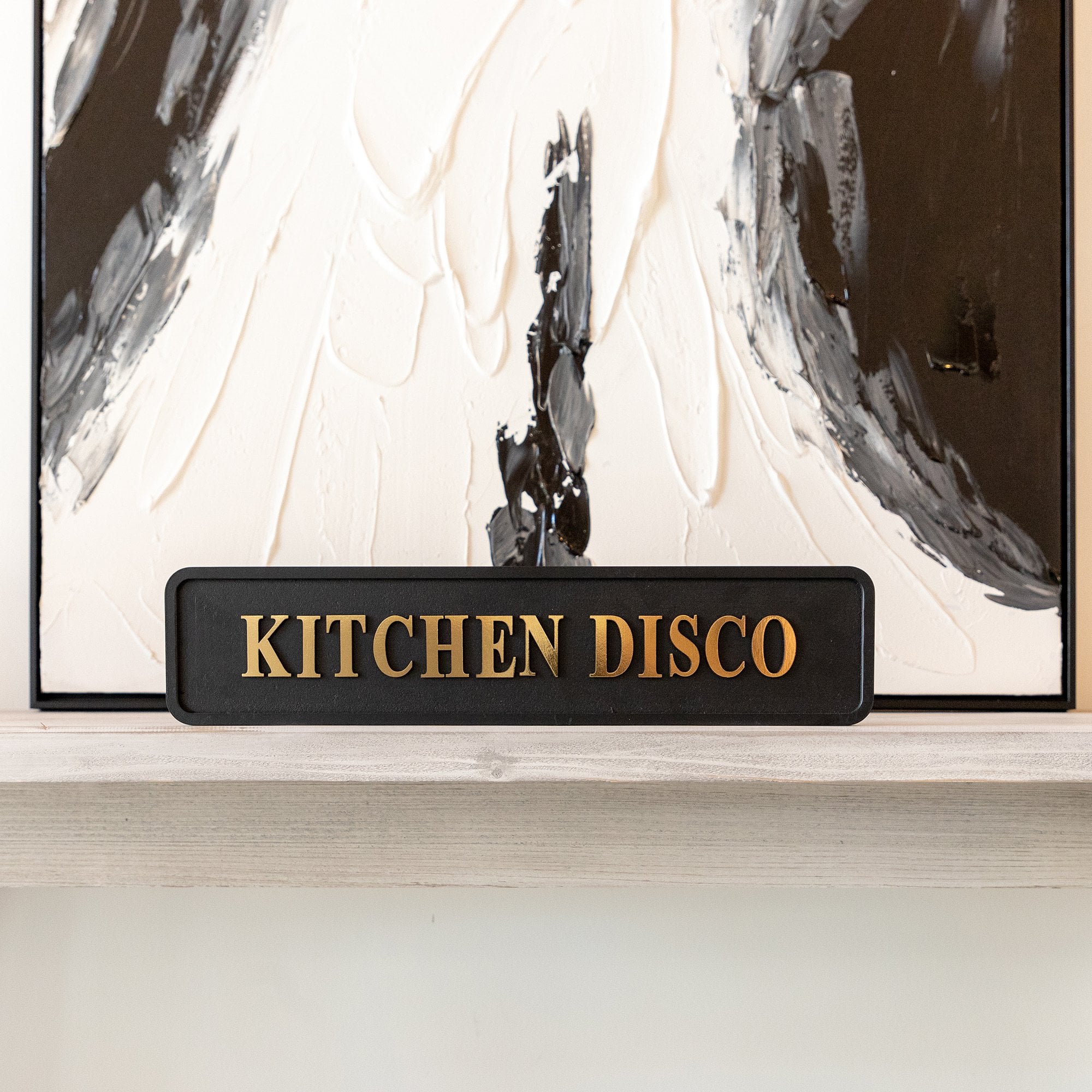 Decorative sign with 'KITCHEN DISCO' text in front of an abstract painting