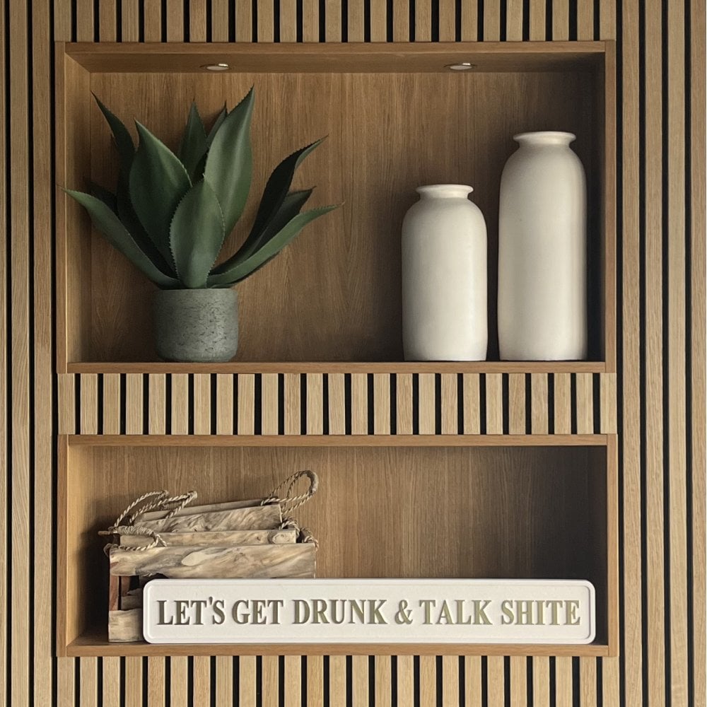 Wooden shelf with decorative items including a plant, vases, and a sign reading 'LETS GET DRUNK AND TALK SHITE' with gold foil letters.