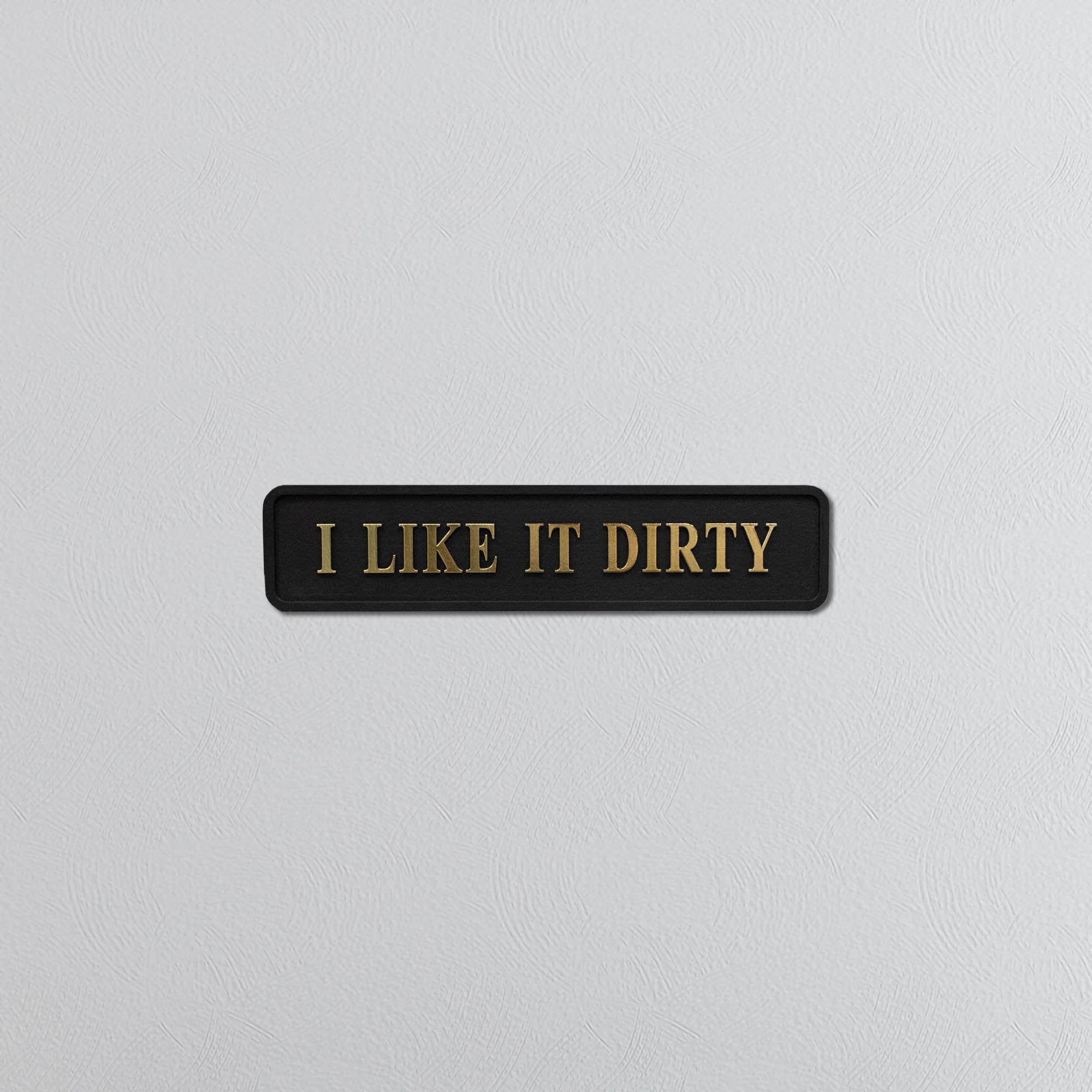 Black sign with gold text 'I LIKE IT DIRTY' on a light gray background