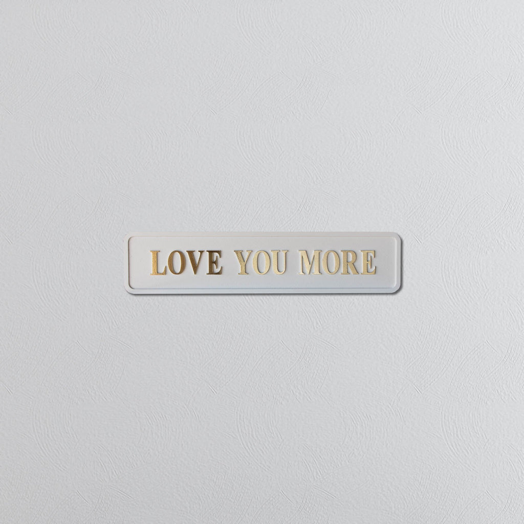 Cream and gold foil plaque with 'LOVE YOU MORE' text on a light gray background
