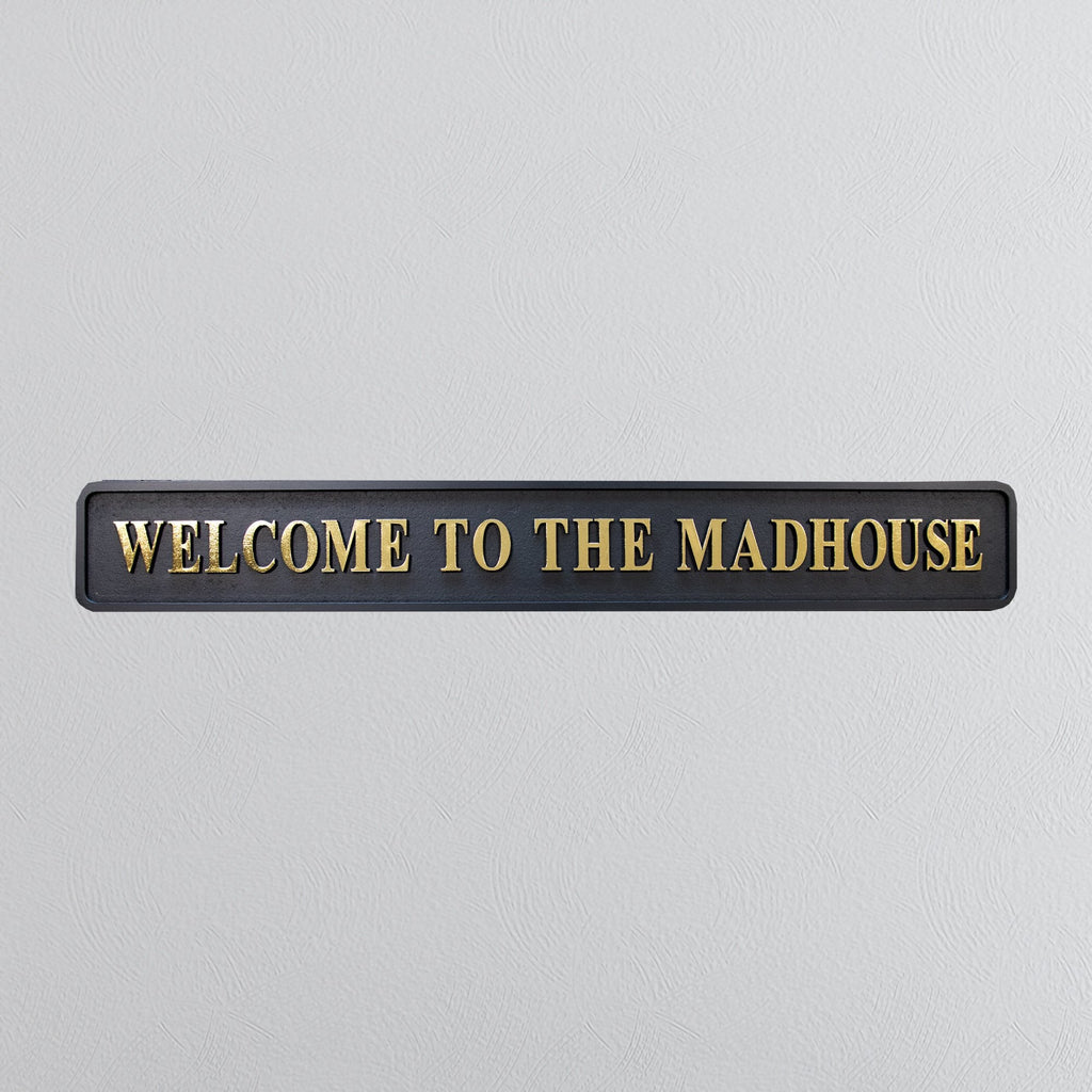 Black and gold foiled street sign with "welcome to the madhouse" wording