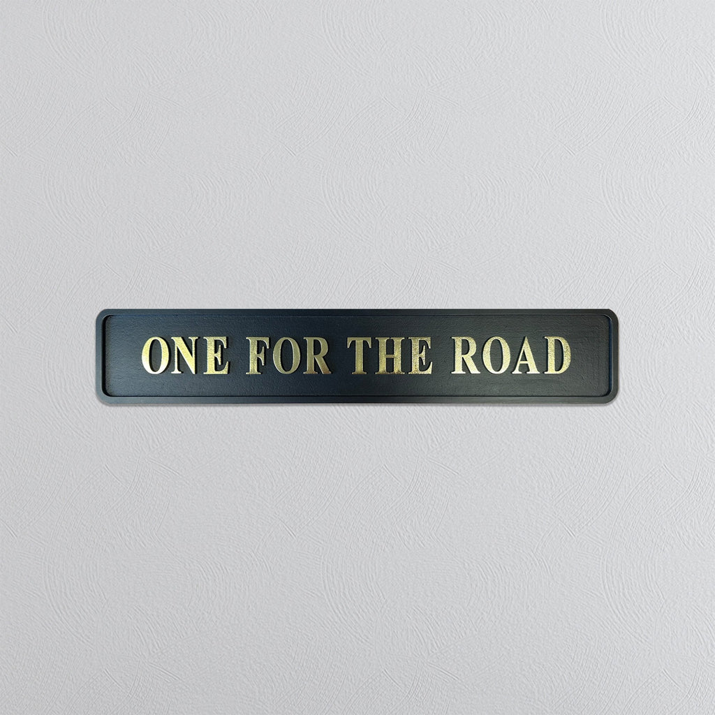Black sign with 'ONE FOR THE ROAD' in gold letters on a light gray background