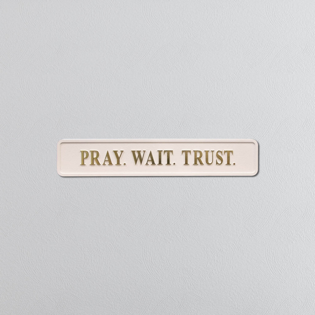 Rectangular sign with 'PRAY. WAIT. TRUST.' text on a light gray background