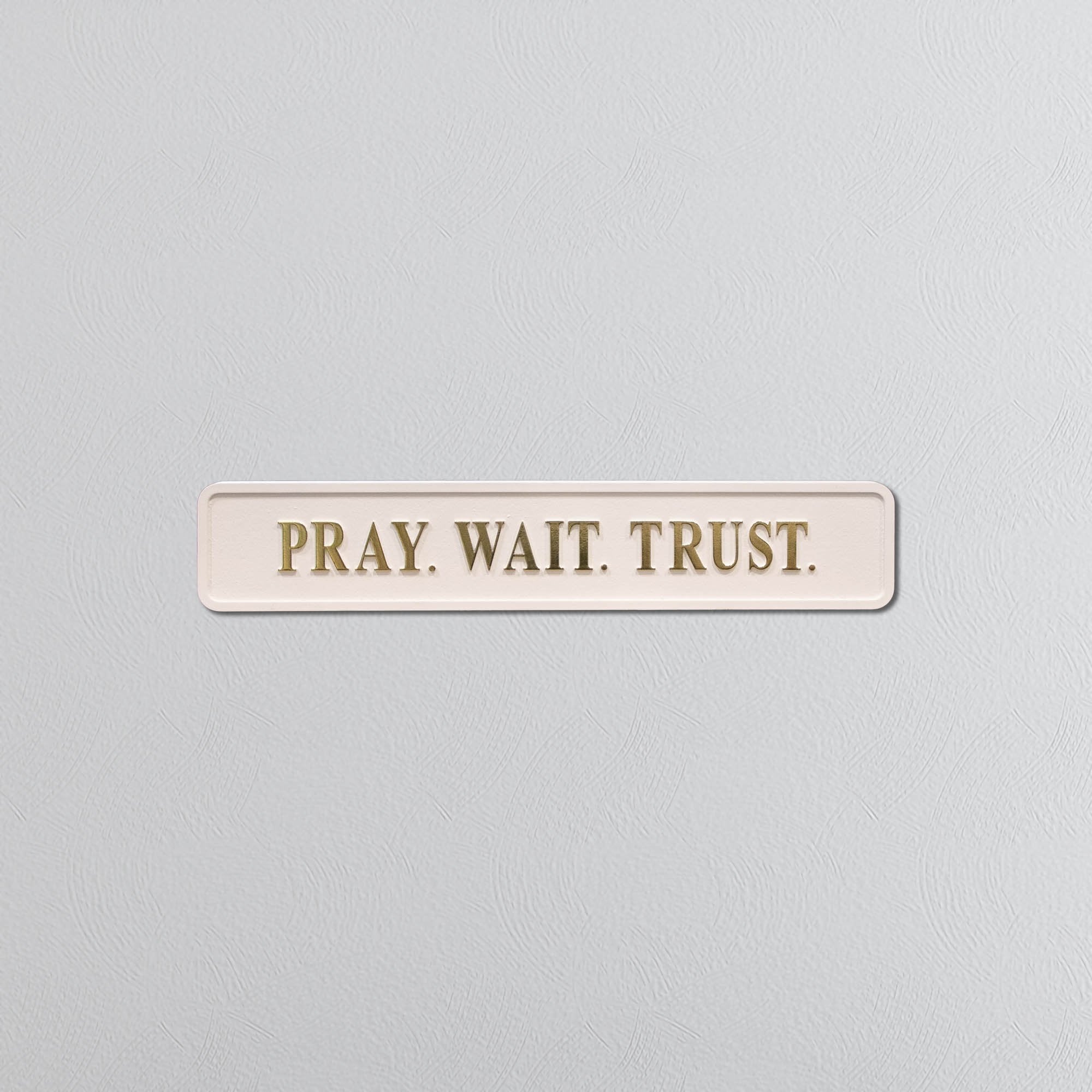 Rectangular sign with 'PRAY. WAIT. TRUST.' text on a light gray background