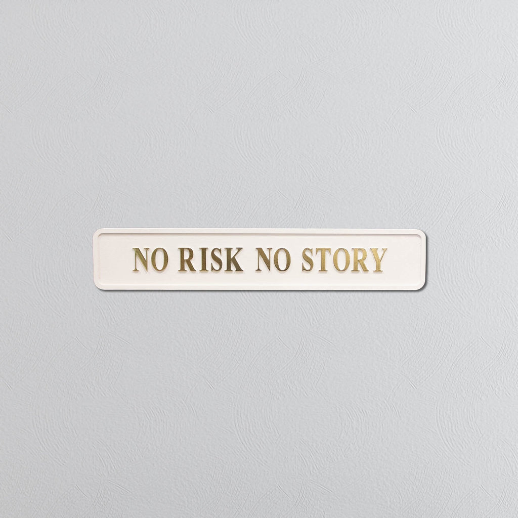 Rectangular sign with 'NO RISK NO STORY' in gold text on a light gray background