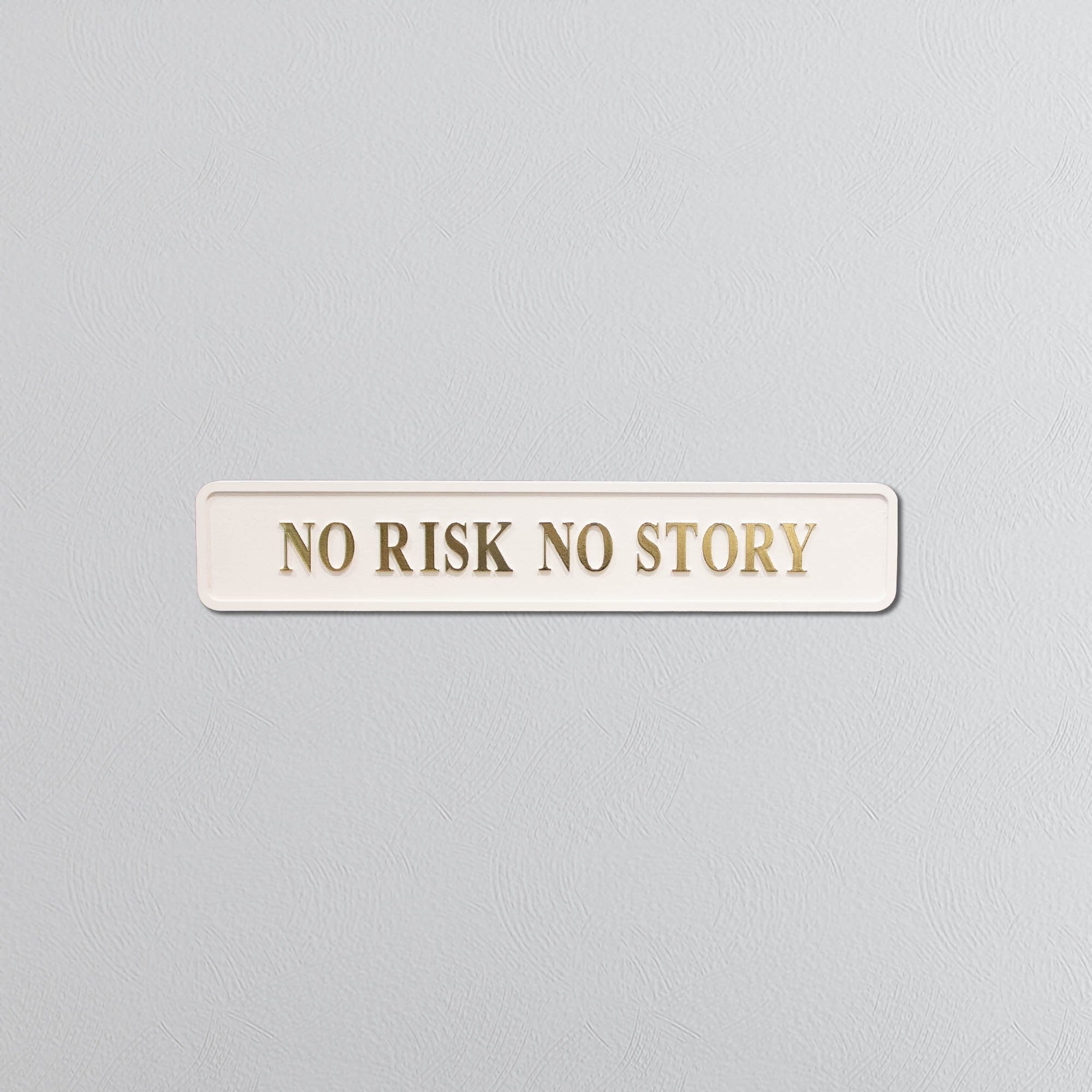 Rectangular sign with 'NO RISK NO STORY' in gold text on a light gray background