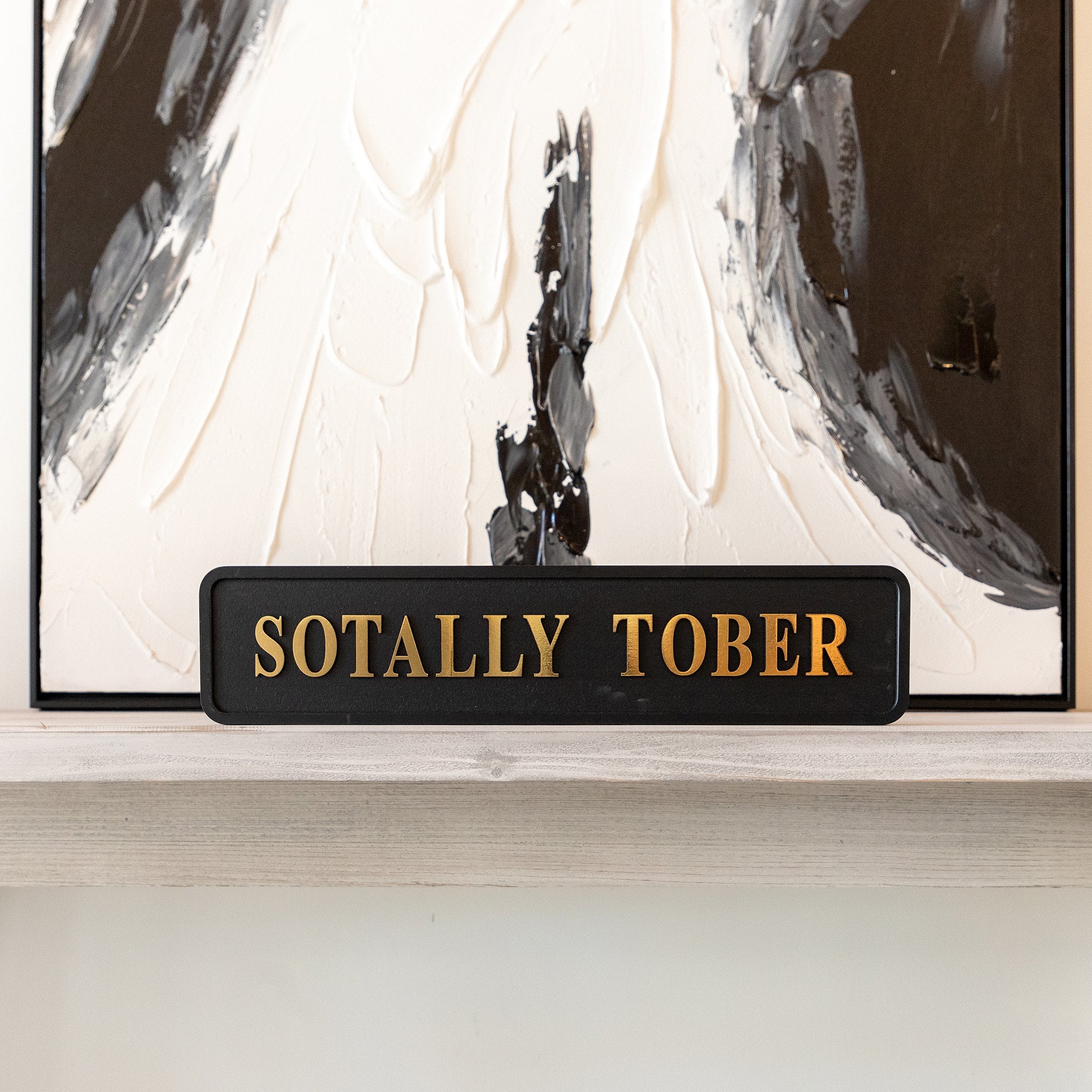 Decorative sign with 'SOTALLY TOBER' text in front of abstract art
