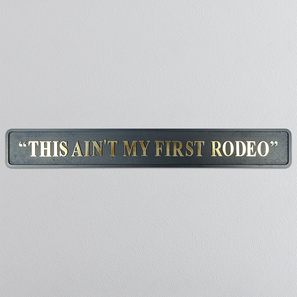 Decorative sign with text 'THIS AIN'T MY FIRST RODEO' on a gray background