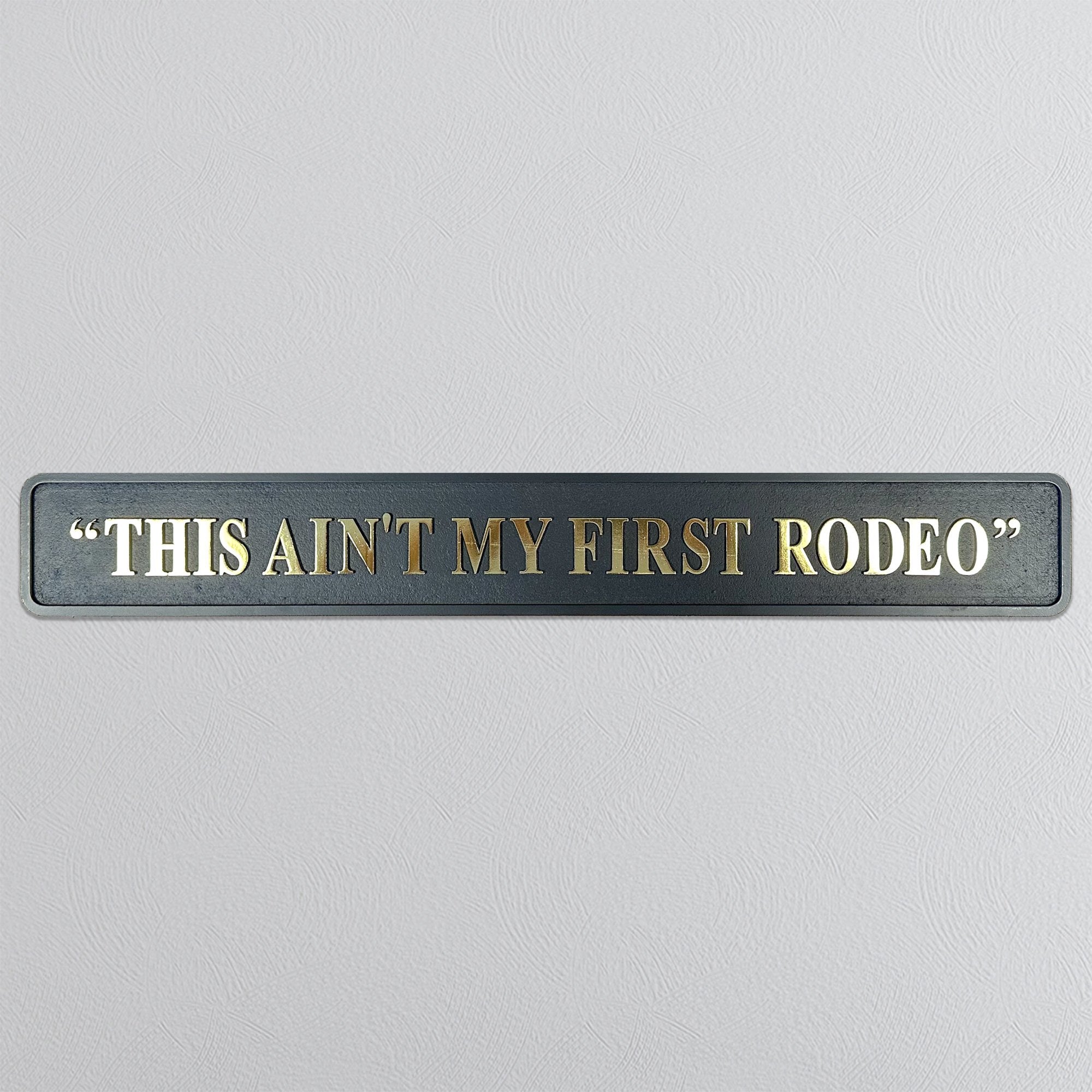 Decorative sign with text 'THIS AIN'T MY FIRST RODEO' on a gray background