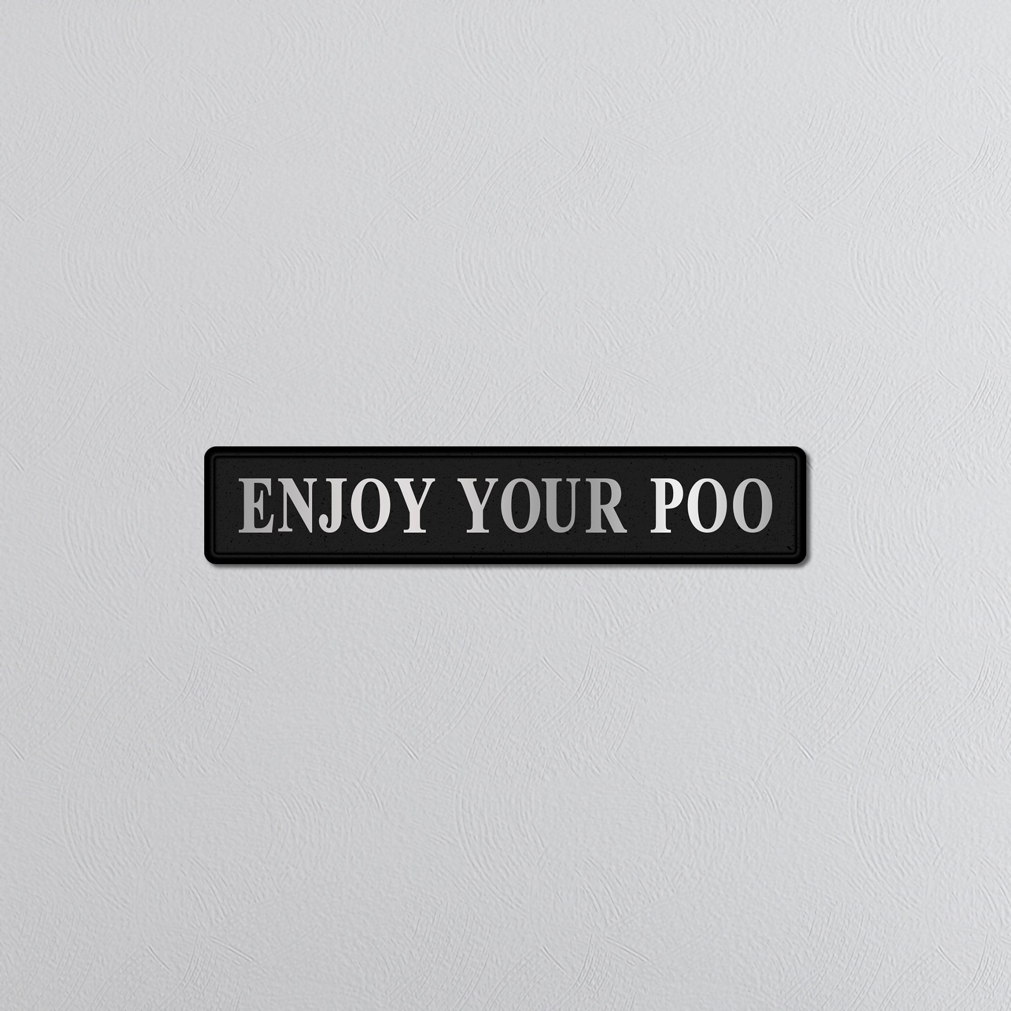 Black sign with silver text 'ENJOY YOUR POO' on a light gray background
