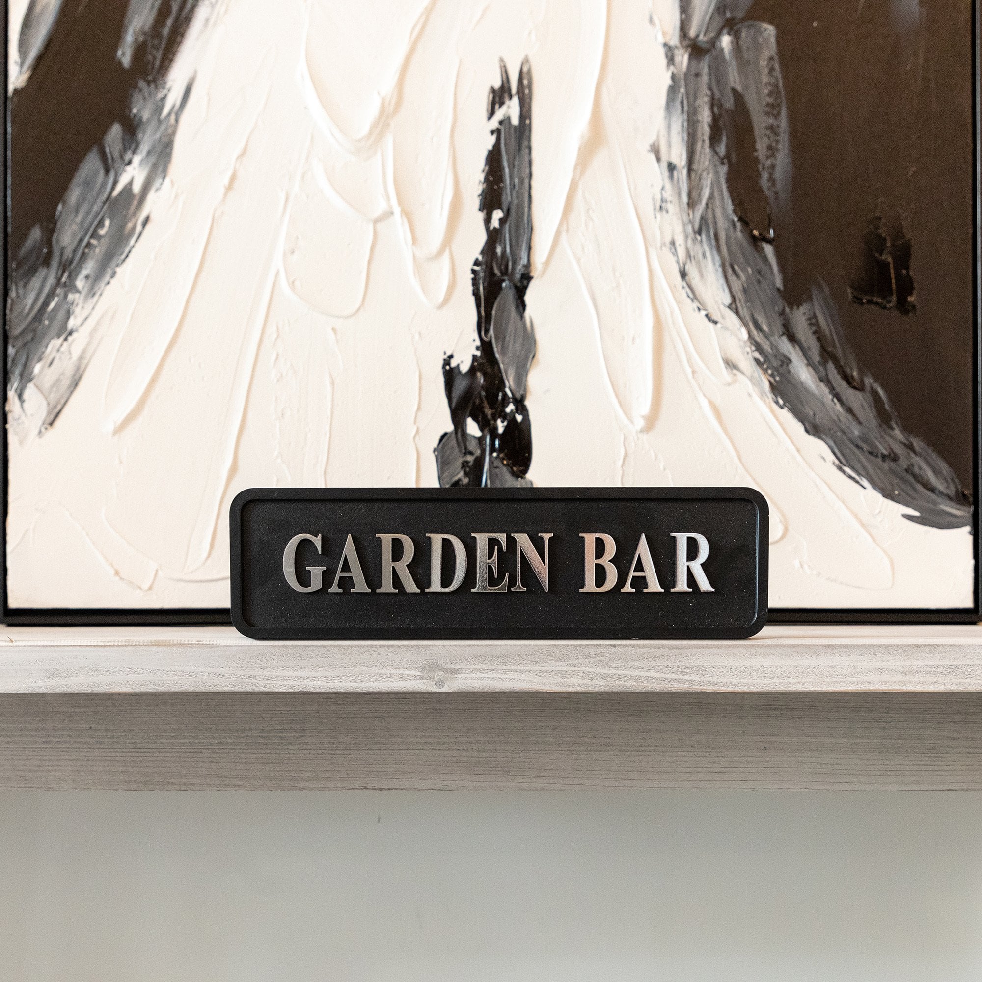 Decorative sign with 'GARDEN BAR' text in front of abstract art