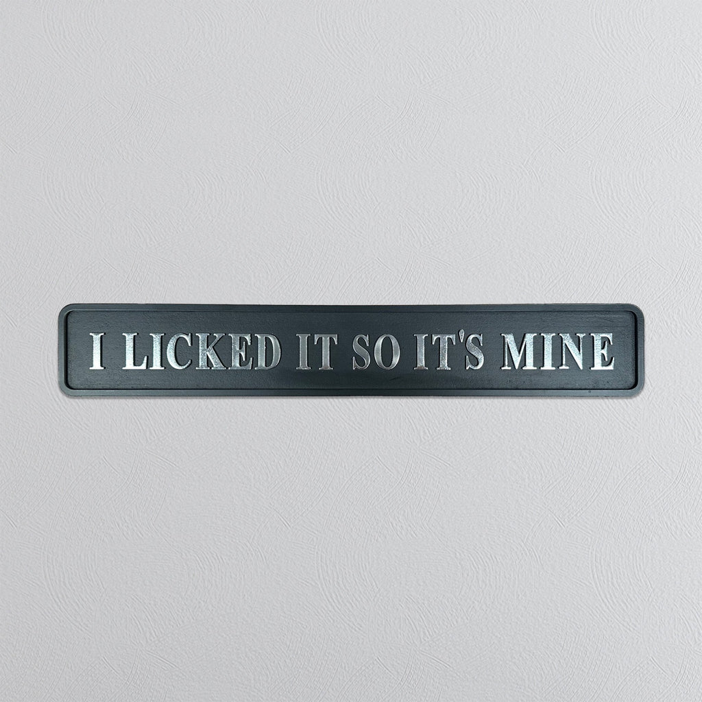 Decorative sign with silver text 'I LICKED IT SO IT'S MINE' on a light gray background