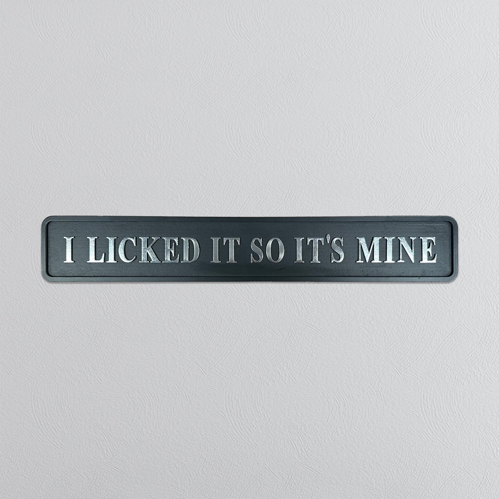 Decorative sign with silver text 'I LICKED IT SO IT'S MINE' on a light gray background