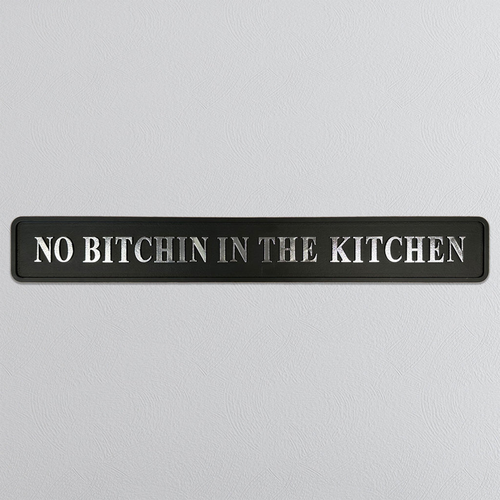 Black sign with silver text 'NO BITCHIN IN THE KITCHEN' on a light gray background