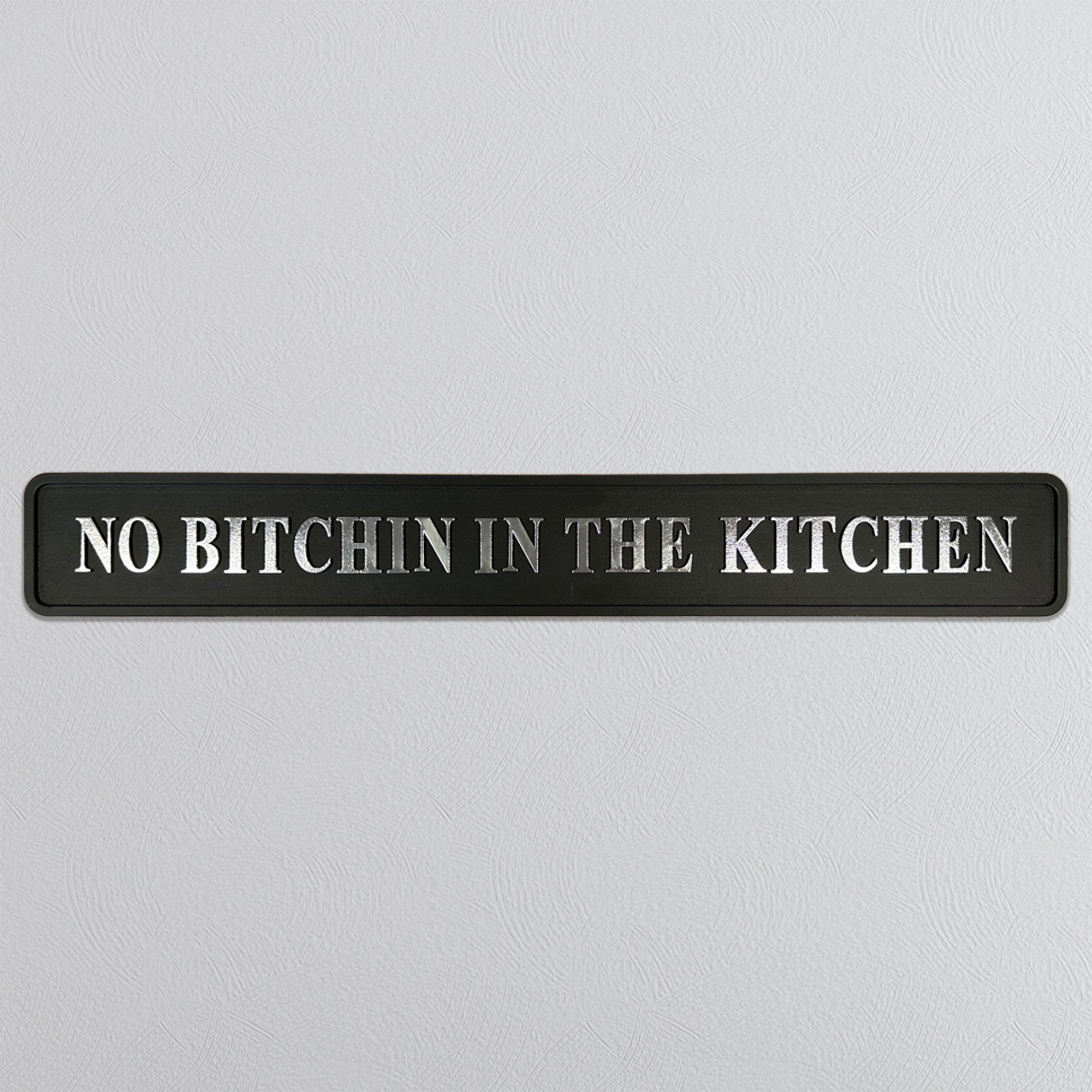 Black sign with silver text 'NO BITCHIN IN THE KITCHEN' on a light gray background