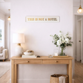 Wooden console table with decorative items in a home setting, featuring a cream and gold sign that reads 'THIS IS NOT A HOTEL'.