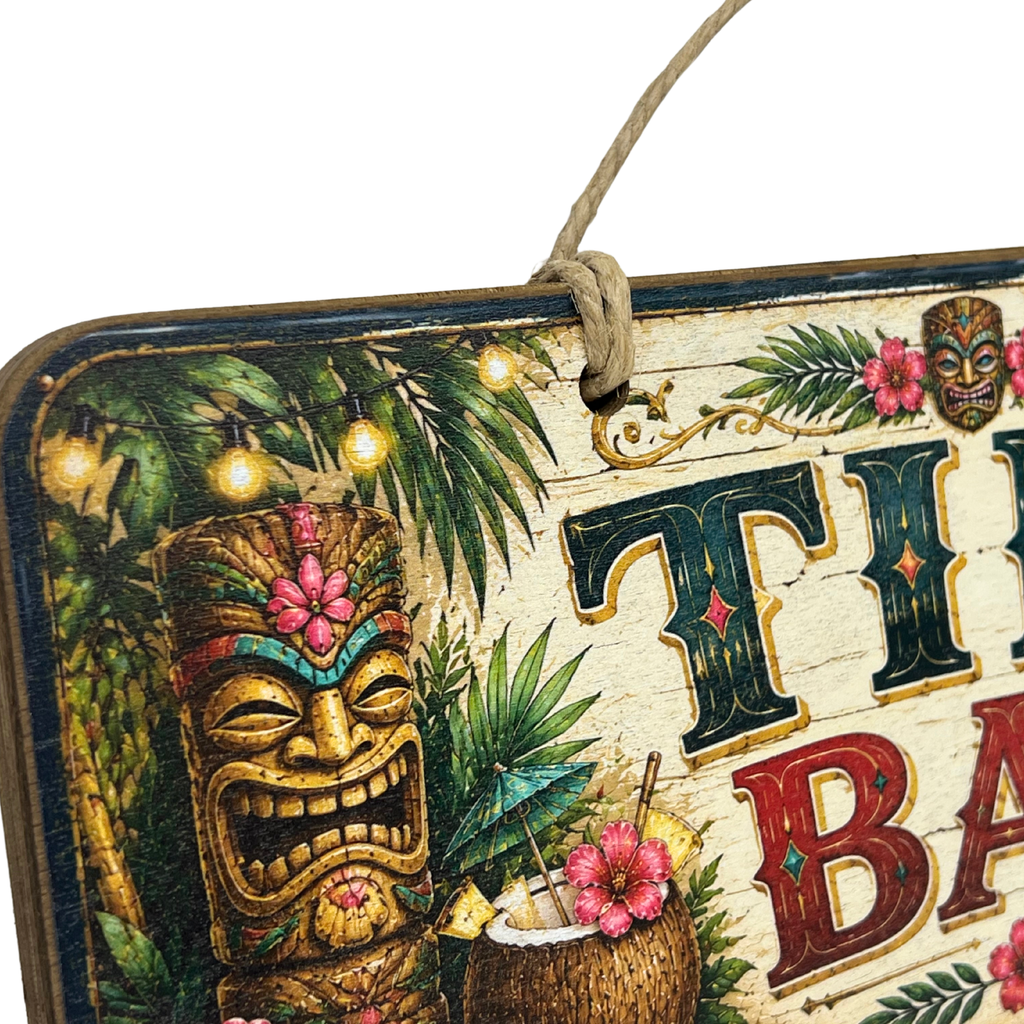 A close-up of a rustic hanging sign with tropical tiki artwork, including a carved tiki figure, palm leaves, flowers, and large decorative letters on a white background.