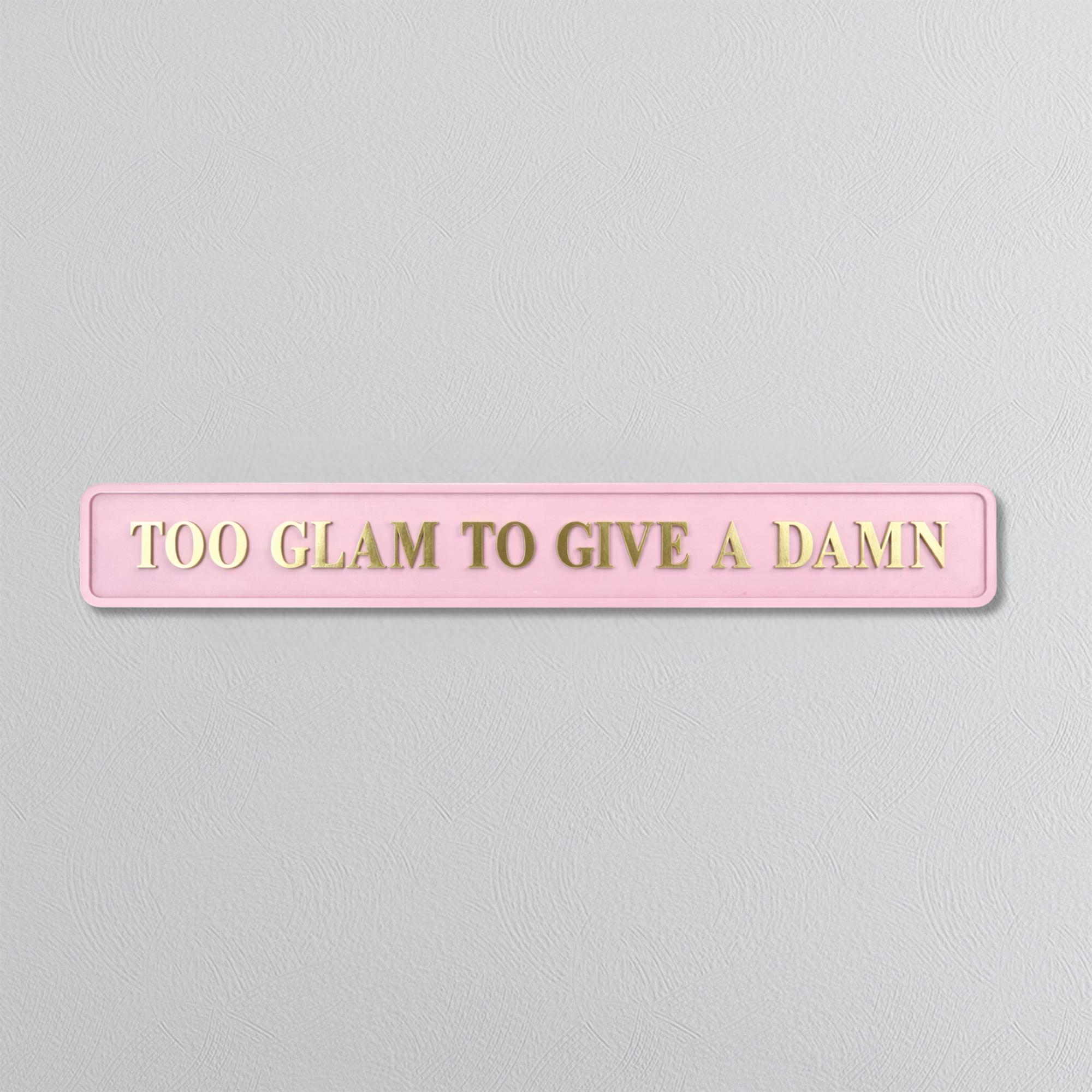Pink sign with gold text 'TOO GLAM TO GIVE A DAMN' on a light gray background
